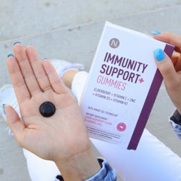 Image of a woman holding an Immunity Support + Gummy in one hand the product packaging in the other.