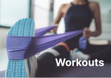 Workouts. A woman in fitness apparel sitting down while using a purple band under her light blue sneakers.