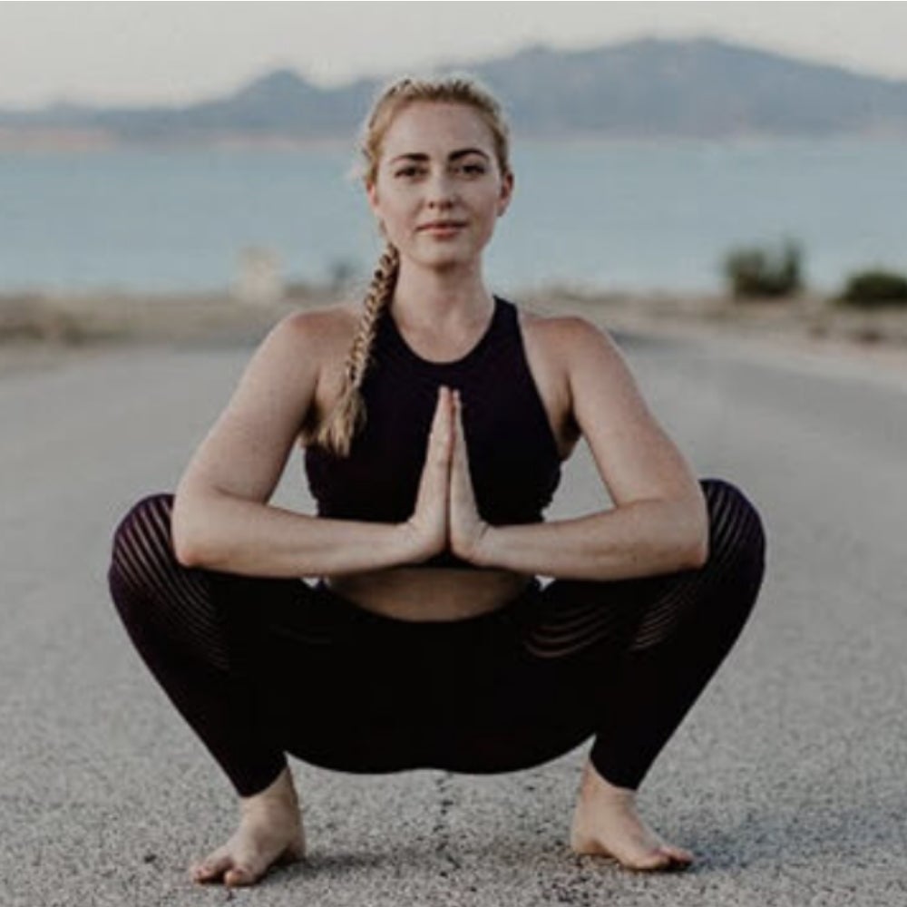 A woman doing a yoga squat pose on concrete.