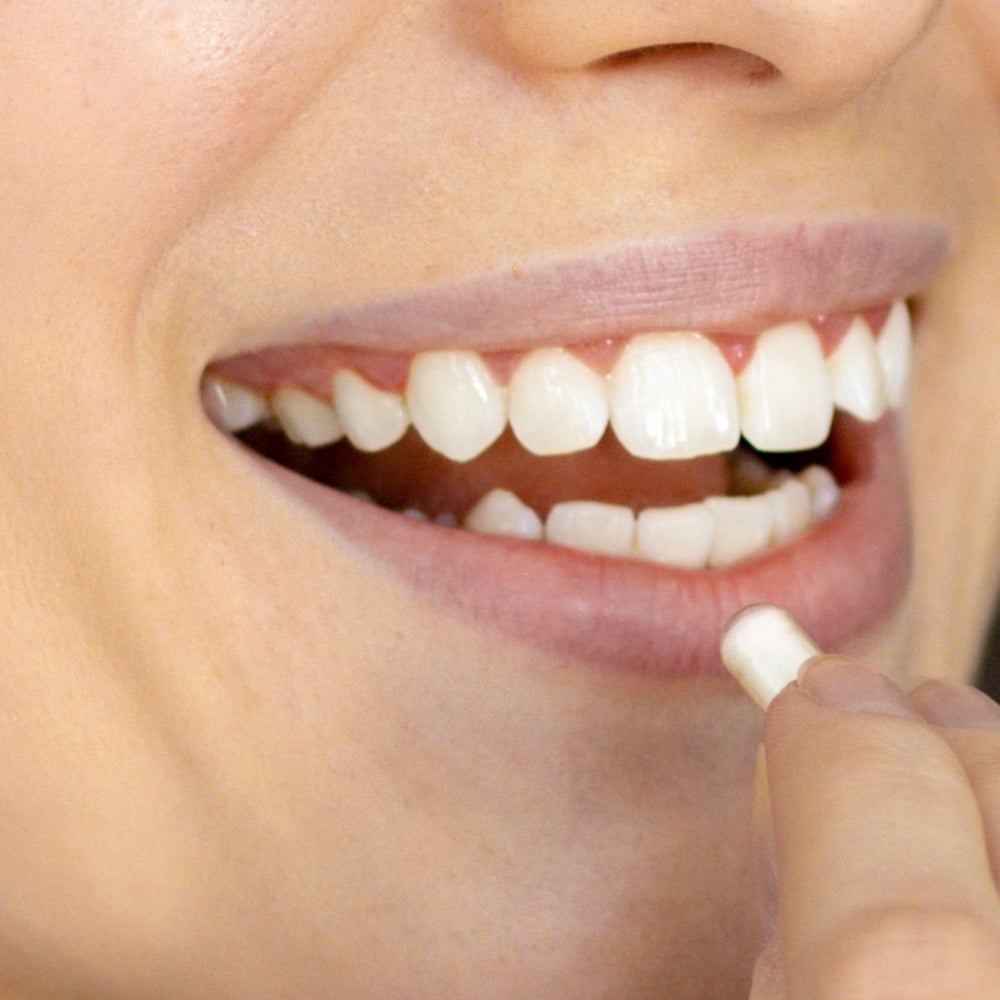 A closeup of a woman’s mouth that’s about to take a white pill.