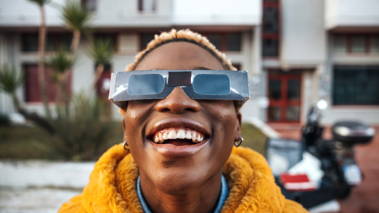 a woman using eclipse glasses to view the eclipsing sun