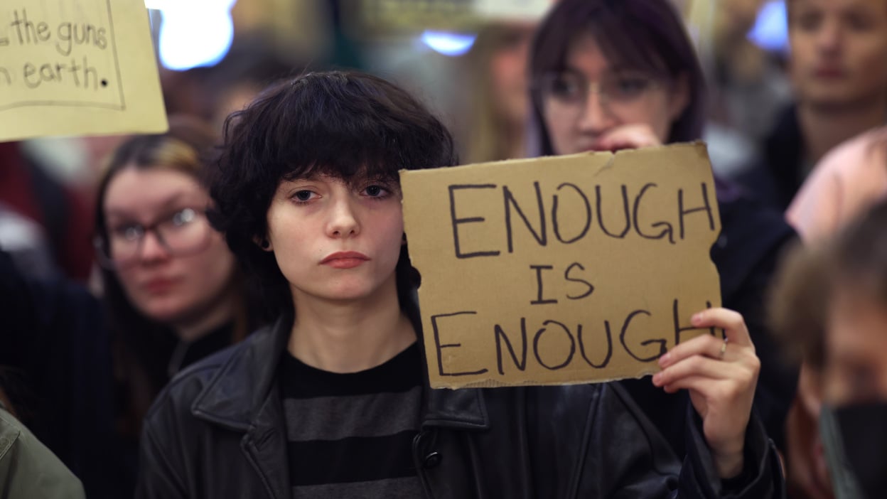 A young person holds up a cardboard sign that reads "Enough is enough."