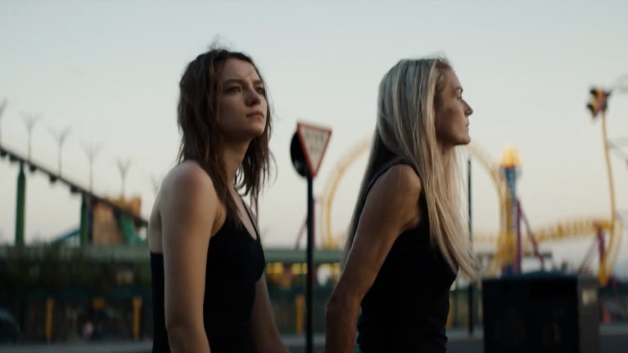 Two women walk through a fairground at sunset.