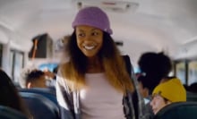 A girl standing in the aisle of a school bus smiling.