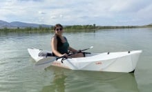 Person with long hair wearing a green top in a white oru kayak on a lake