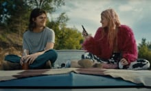 A couple sit on the hood of a car.