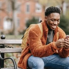 man sitting on park bench and smiling at his phone