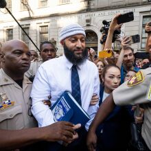 A man walks out of the court house surrounded by police and media.