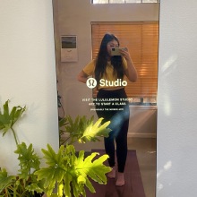 Person with long hair wearing black leggings and a yellow shirt standing in front of a Lululemon Studio Mirror