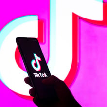  In this photo illustration, a woman's silhouette holds a smartphone with the TikTok logo displayed on the screen and in the background.