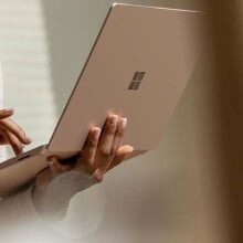 The Microsoft Surface Laptop 3 in a rose gold color held up while someone while they're standing