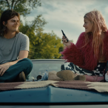 A couple sit on the hood of a car.