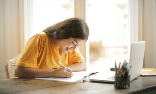 Girl writing in front of laptop