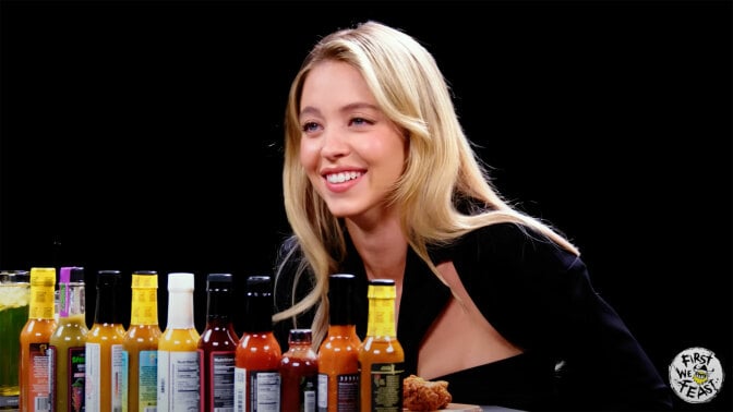 A woman sits at a table in a dark room with sauce bottles in front of her.