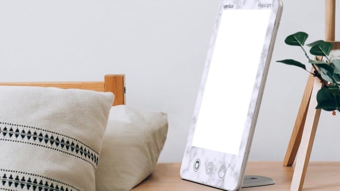 a verilux happylight luxe sits on a bedside table