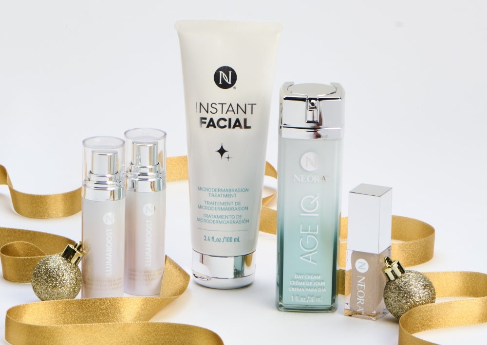 IllumaBoost bottles, Neora’s Instant Facial tube, Age IQ Day Cream, and a Neora Shimmer Lip Oil container are surrounded by gold ribbon and ornaments. Accompanying text states “Free Gift!” And “Save 20%.”