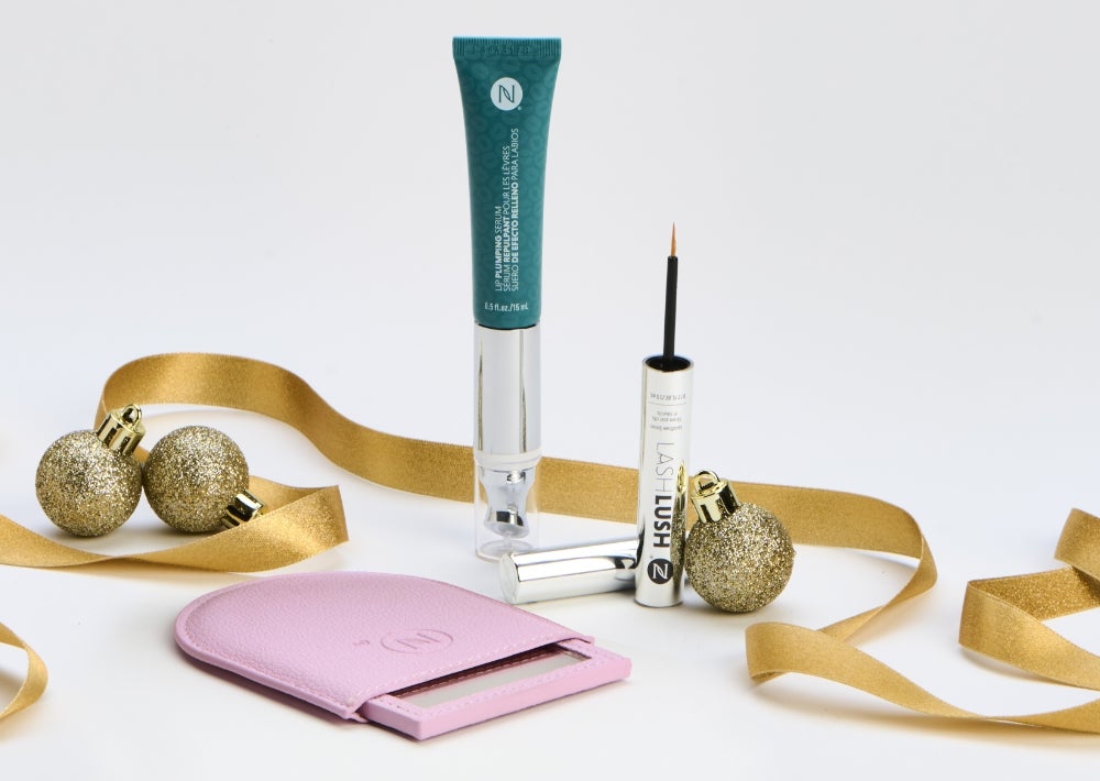 A Lip Plumping Serum and LashLush tube are surrounded by gold ribbon, ornaments and a pink purse mirror. Accompanying text states “Free Gift!” And “Save 20%.”