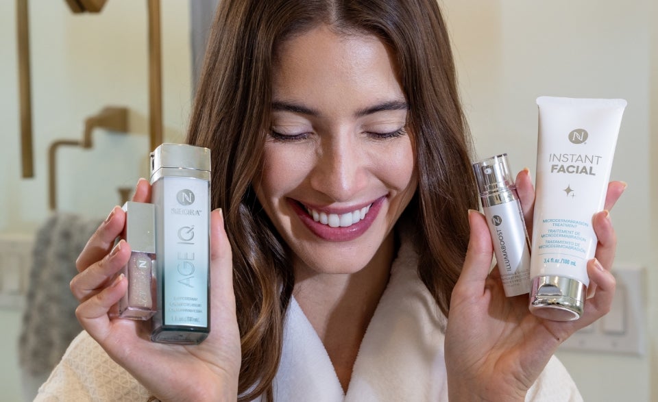 A woman holds up Age IQ Day Cream in her right hand and a tube of Instant Facial in her left hand next to her face.