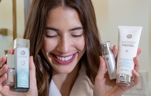 A woman holds up Age IQ Day Cream in her right hand and a tube of Instant Facial in her left hand next to her face.