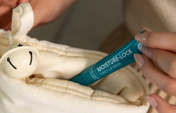 A close-up of a woman’s hand pulling a Moisture-Lock Lip Mask tube out of her bag.