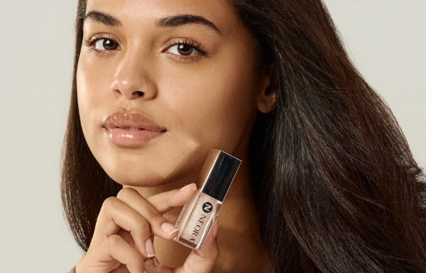 A close-up of a woman pouting next to a container of Neora’s Shimmer Lip Oil.