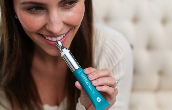 A smiling woman holding the Lip Plumping Serum to her face.