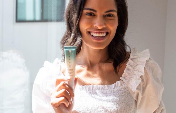 A woman holding an Invisi-Bloc SPF bottle in a well lit room.