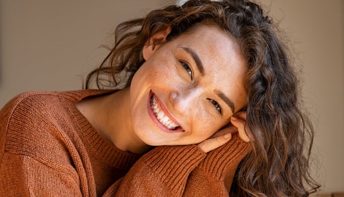 Image of woman smiling with her head in her hands 