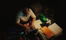 A man looks over a stack of papers in a dimly-lit attorney's office. 