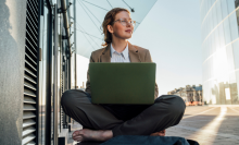 Thoughtful businesswoman sitting cross-legged with laptop on bench