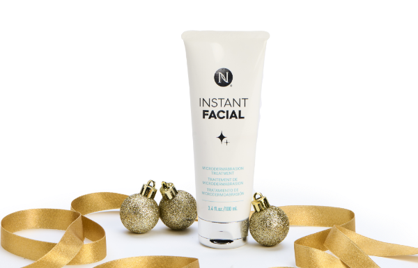 A tube of Neora’s Instant Facial surrounded by gold ribbon and ornaments. Accompanying text states “NEW!” and “Holiday Exclusive.”