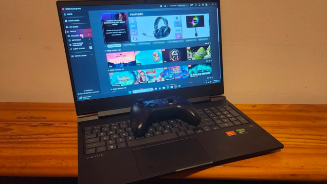 an hp victus 16 sitting on a wooden surface with a black gaming controller on top of it